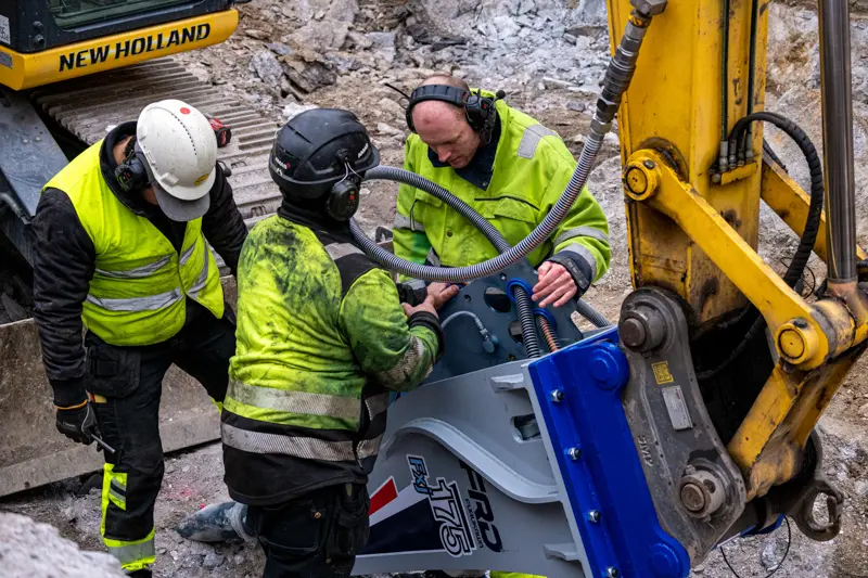 Tre män tittar in under inspektionsluckan på hydraulhammaren.
